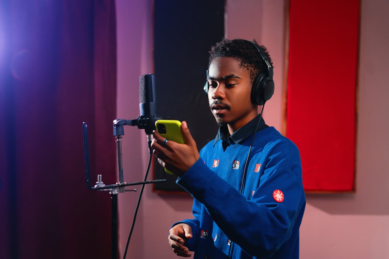 A young musician in a studio recording vocals with a microphone and headphones.