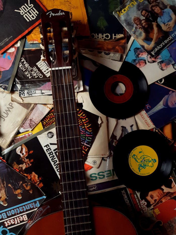 Top view of acoustic guitar placed on top carton packages of vinyl disks with music of 80s