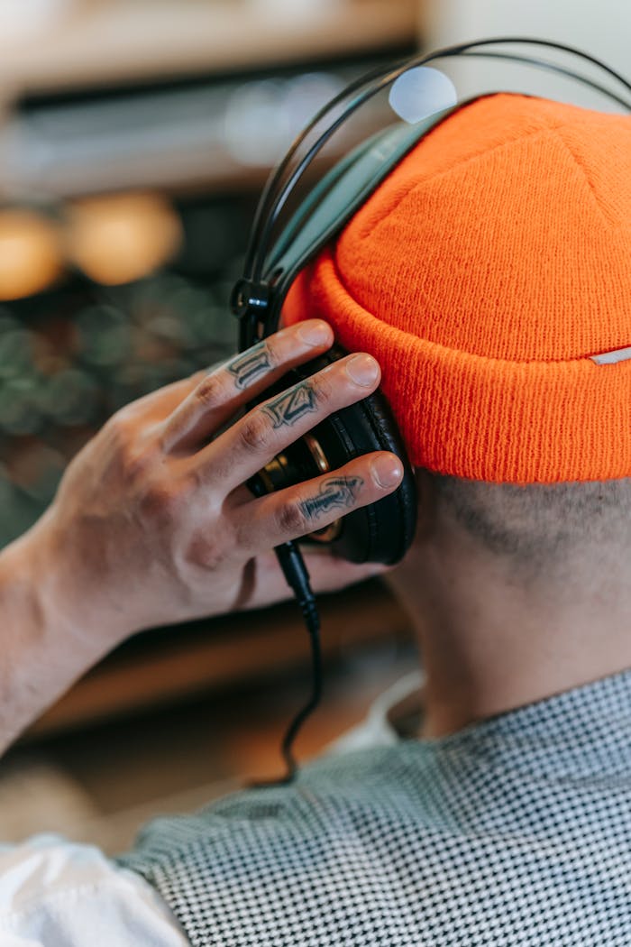 Back view of a man with tattoos wearing headphones and an orange beanie in a music environment.