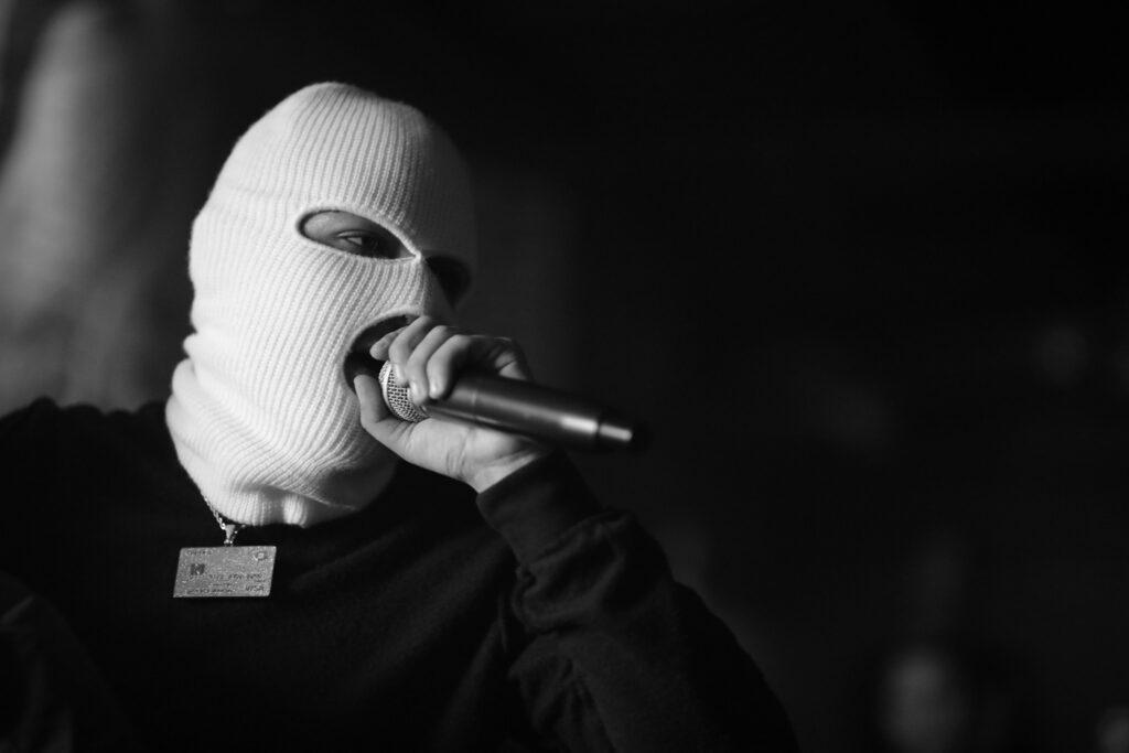 A masked musician passionately singing into a microphone during a live performance.