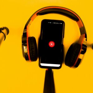 A smartphone with wireless headphones and microphone set against a vibrant yellow background.