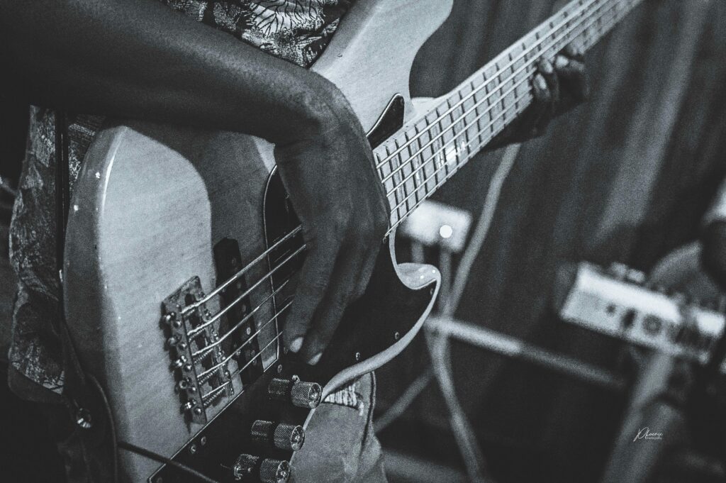 A black and white shot of a musician playing an electric guitar, focusing on hand and strings.